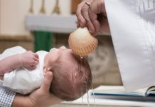 Padrinho segurando bebê durante cerimônia de batismo na Igreja Católica.