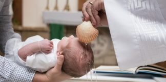 Padrinho segurando bebê durante cerimônia de batismo na Igreja Católica.
